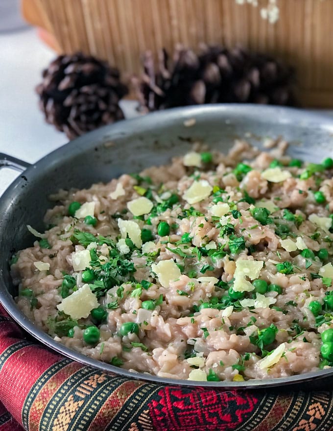 a skillet with risotto and peas topped with parsley and parmesan