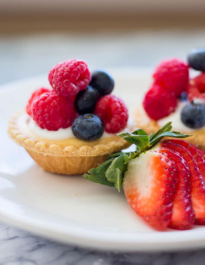 a mini tart piled with raspberries and blueberries on a plate with a sliced strawberry