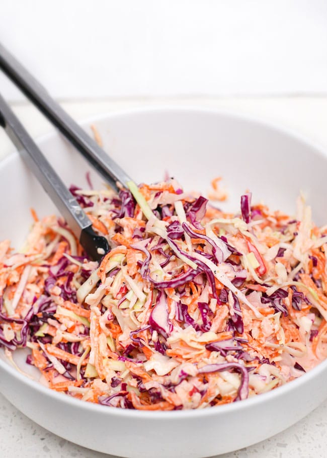 a bowl of apple coleslaw with tongs