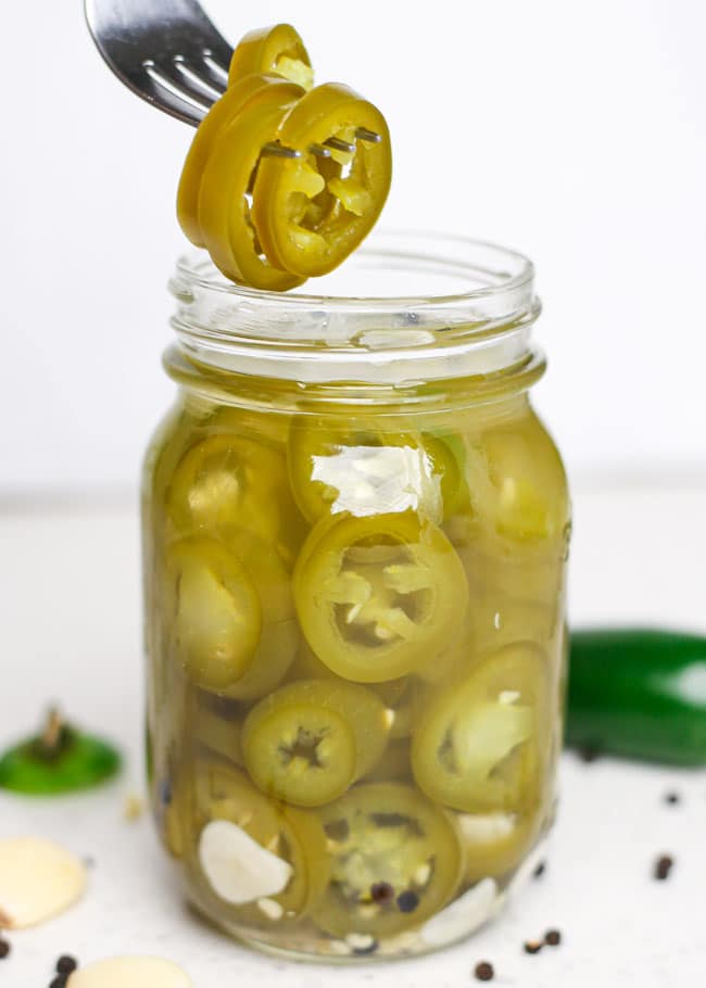 a jar of pickled jalapeno peppers with a fork taking some out