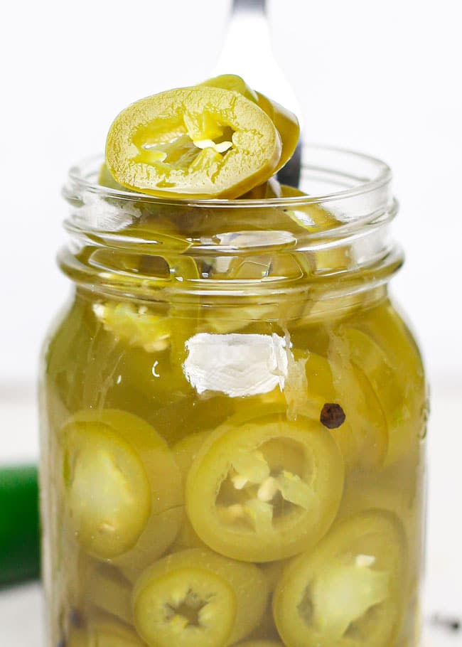 a jar of pickled jalapeno peppers with a fork lifting some out
