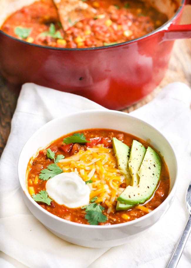 a bowl of turkey chili topped with cheese, cilantro, sour cream, and avocado