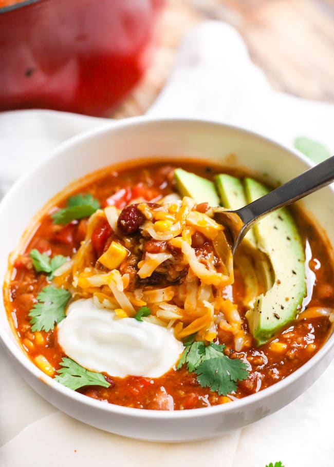 a spoonful of turkey chili and melted cheese topped with cilantro, sour cream, and avocado