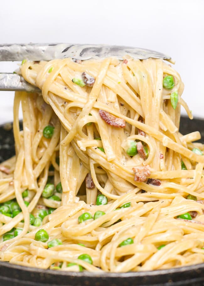tongs picking up creamy pasta with bacon and peas