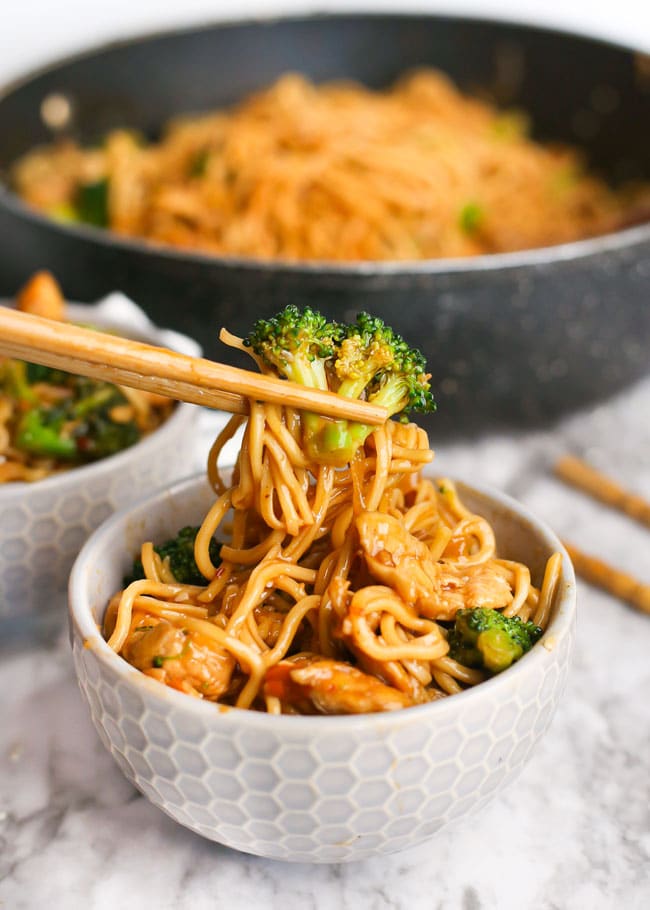 wooden chopsticks holding chicken broccoli stir fry and noodles from a bowl