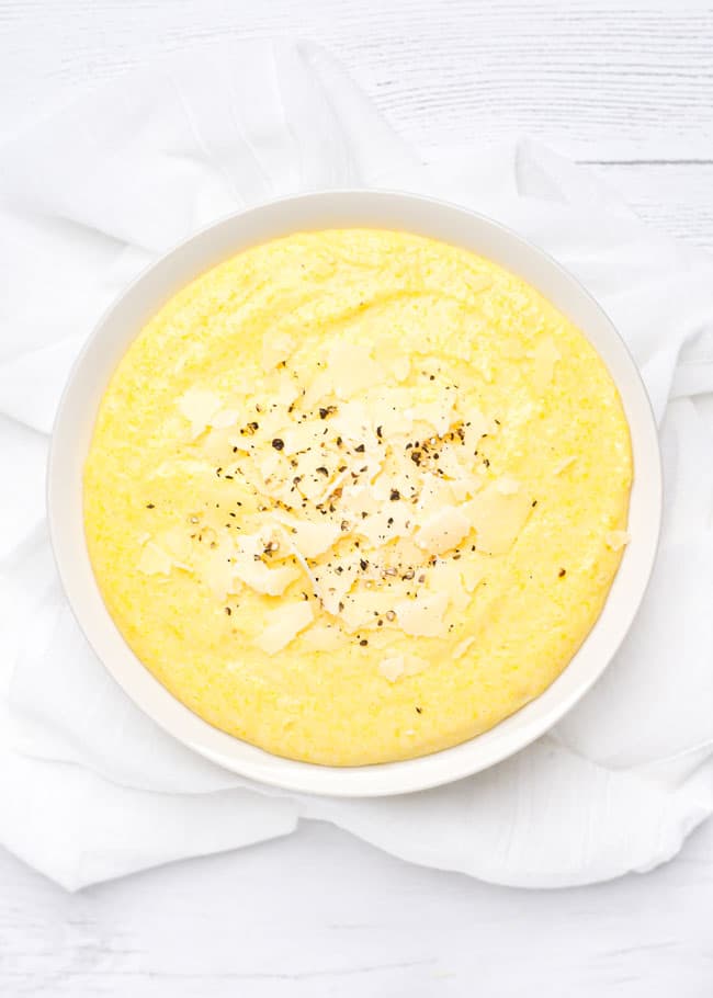 overhead shot of a bowl of creamy polenta topped with parmesan cheese and pepper.