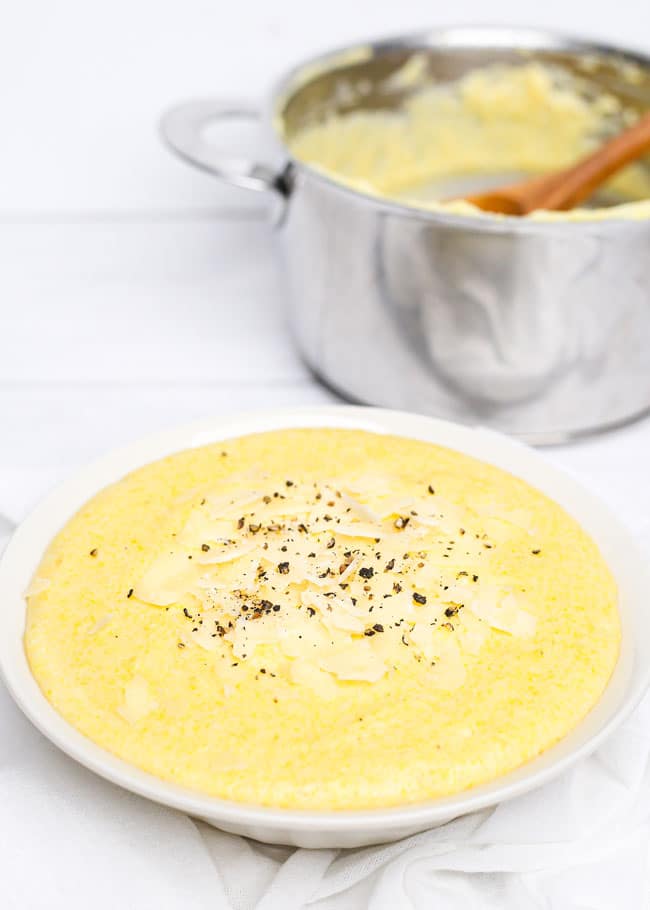 a bowl of creamy polenta with a pot in the background