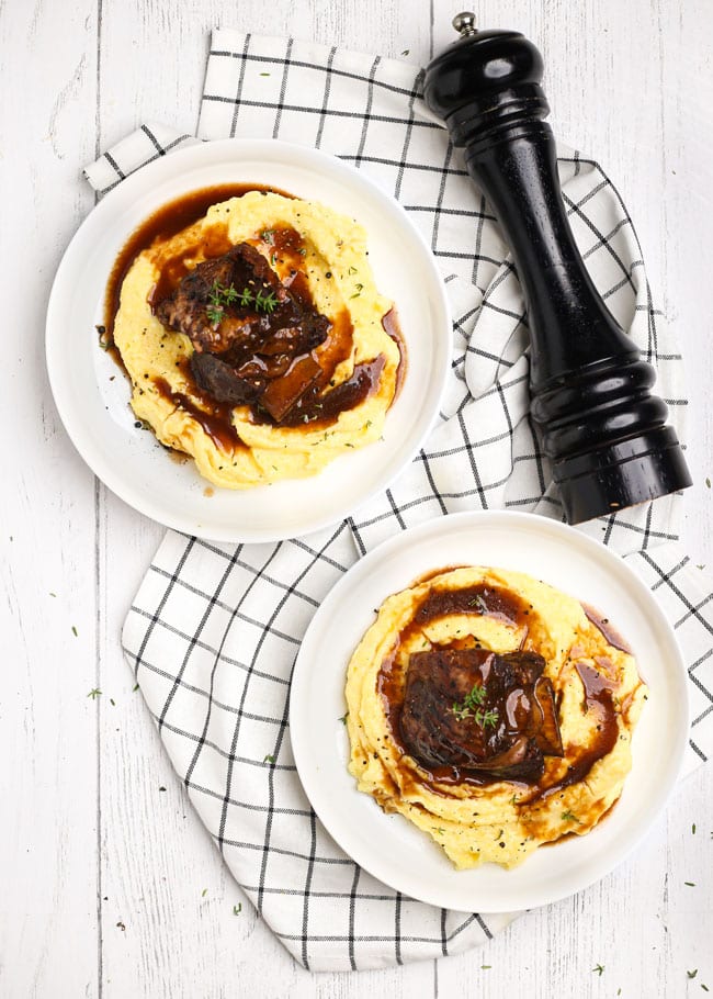 overhead shot of two plates with short ribs over polenta with sauce
