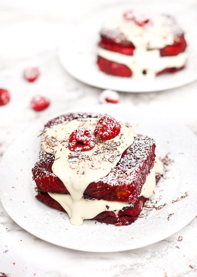 a stack of red velvet french toast with cream cheese icing and raspberries