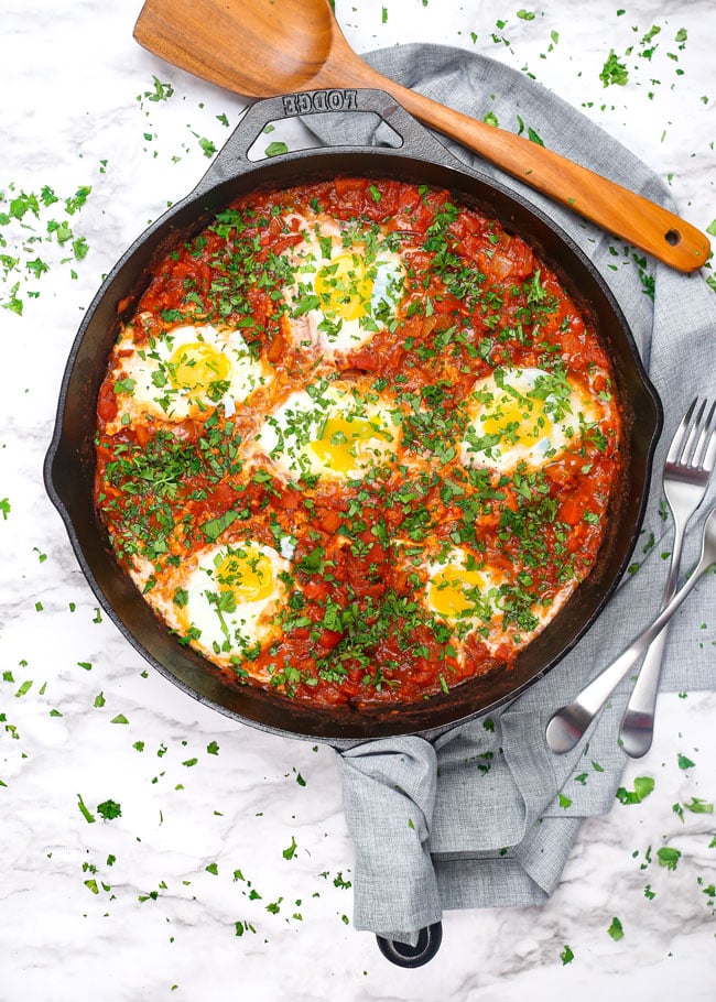 overhead photo of a skillet of shakshuka with poached eggs and a spatula
