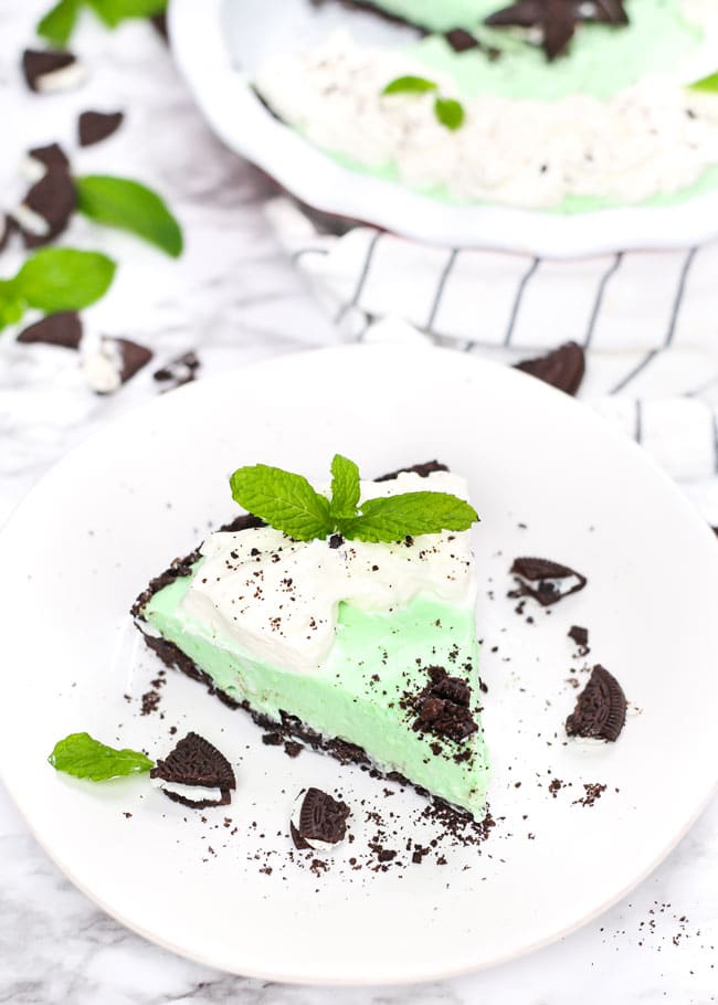 a slice of grasshopper pie on a plate with oreos, whipped cream, and fresh mint