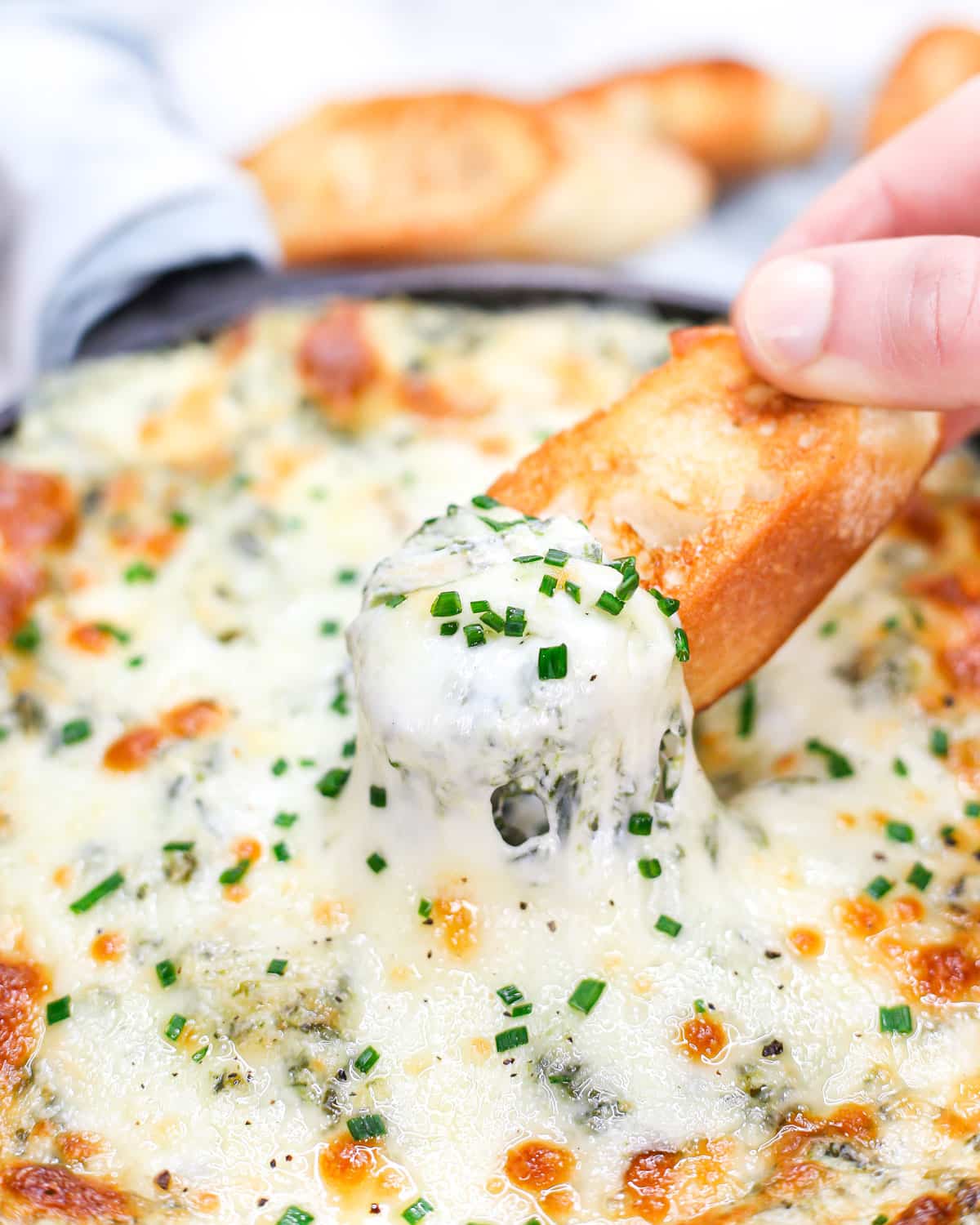 a crostini pulling cheesy spinach artichoke dip from a skillet