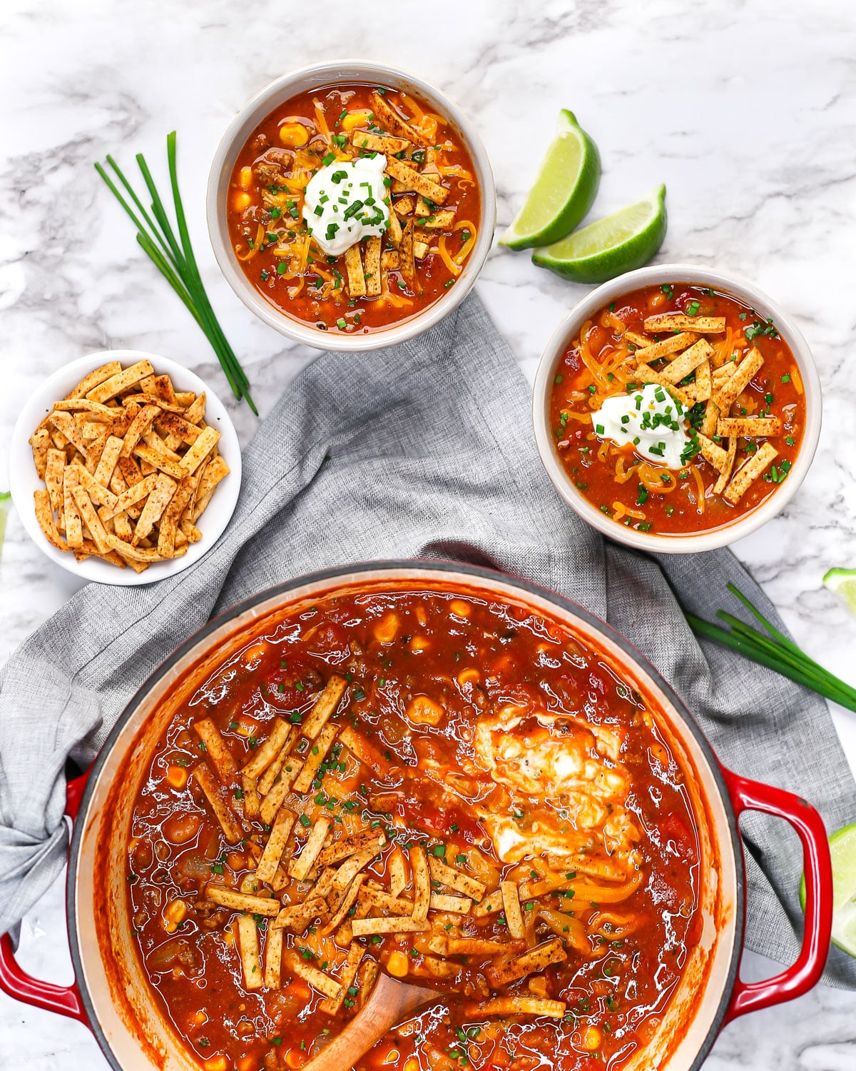 overhead shot of bowls of taco soup being served topped with sour cream, tortilla strips, cheese, and chives