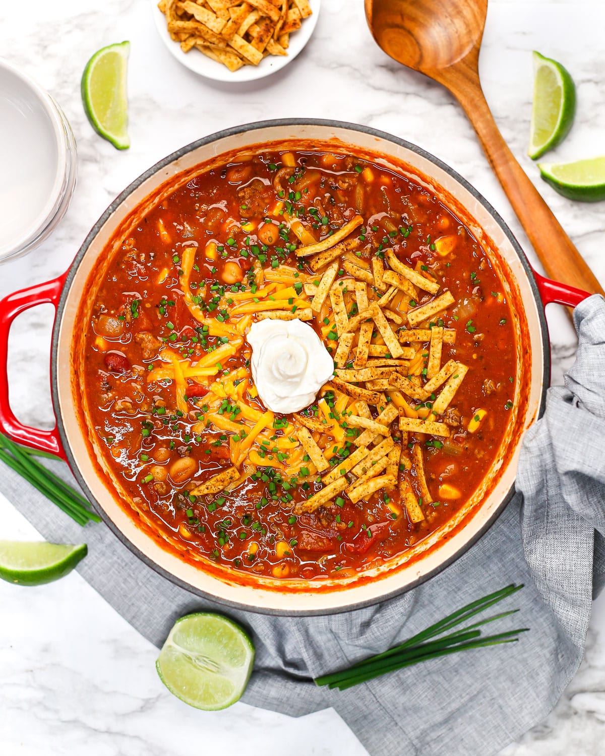 overhead shot of a pot of taco soup topped with cheese, sour cream, chives, and tortilla strips