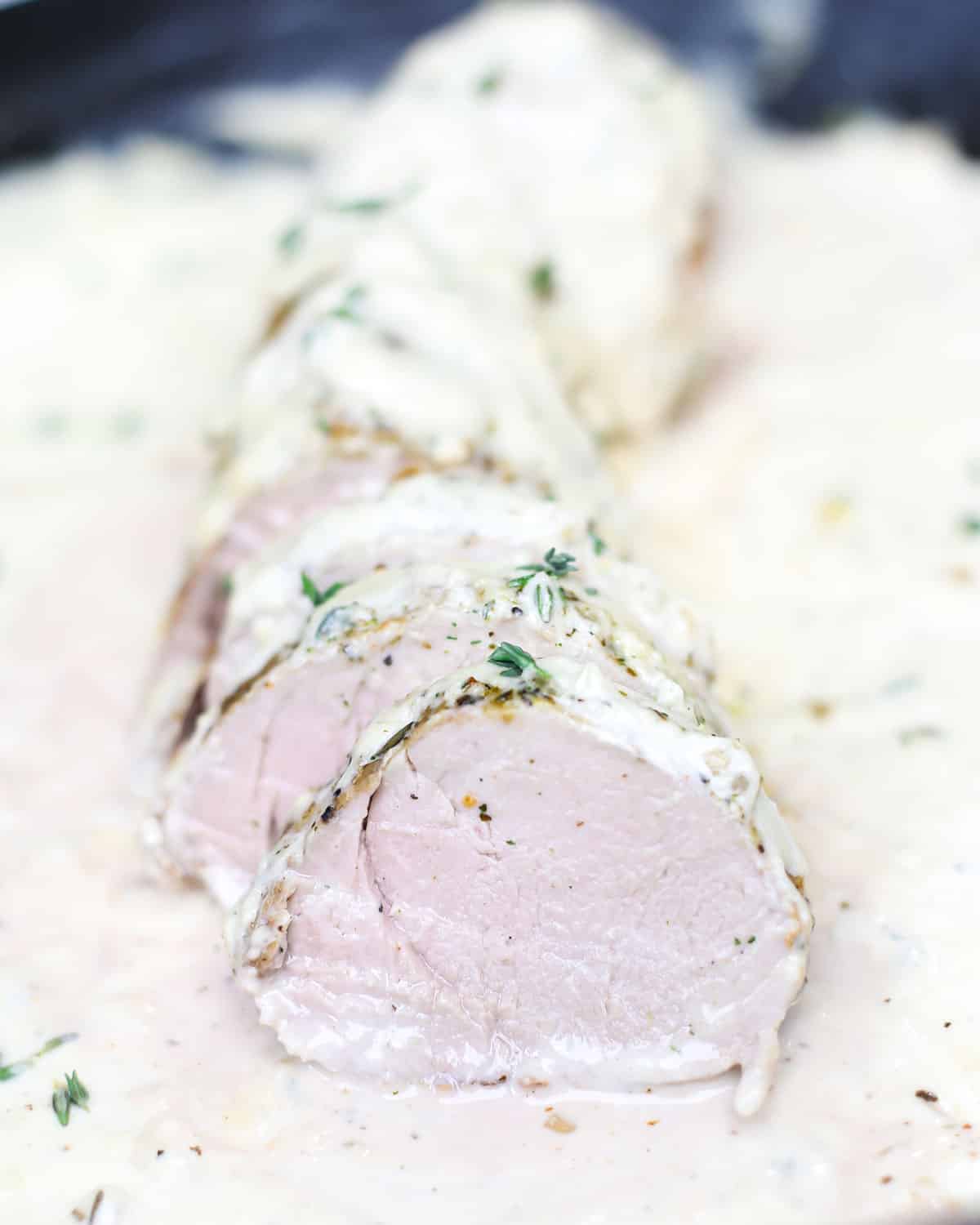 a slice of roasted pork loin topped with cream sauce and thyme