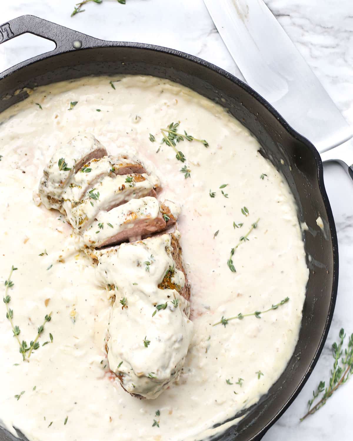 overhead photo of roasted pork loin in a skillet sliced and topped with cream sauce