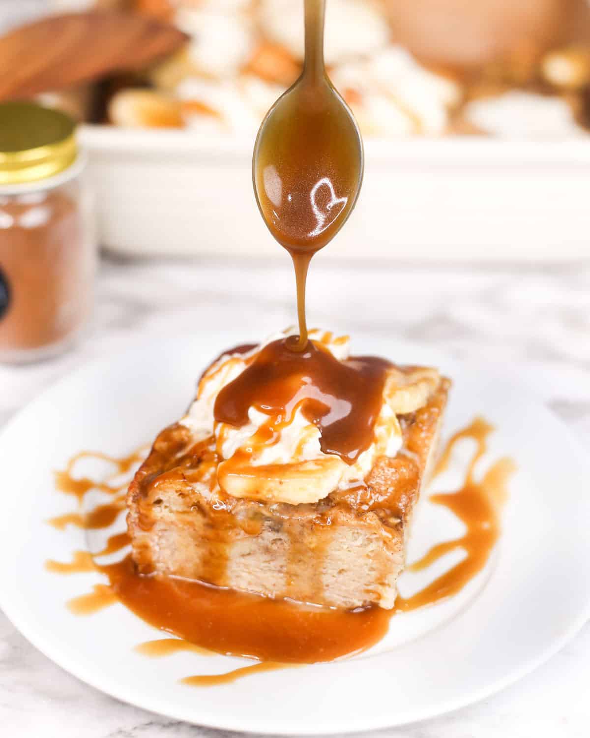 a spoon drizzling caramel sauce over a plate of banana bread pudding