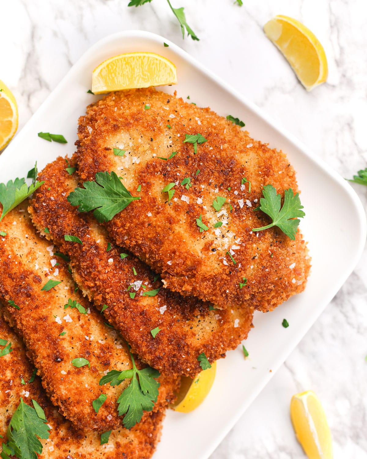 classic pork schnitzels on a plate with lemon wedges and parsley