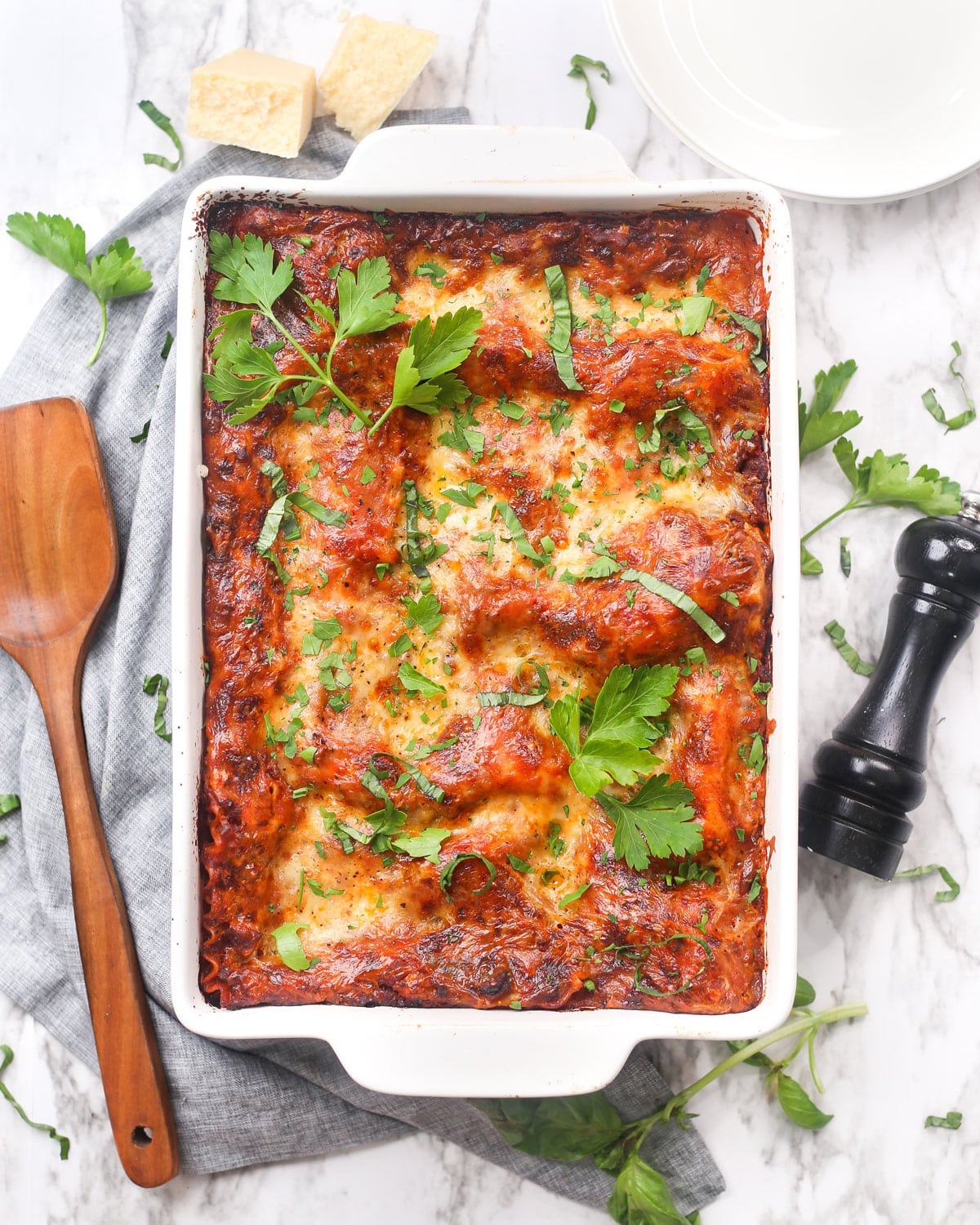 a casserole dish of lasagna garnished with fresh parsley and basil