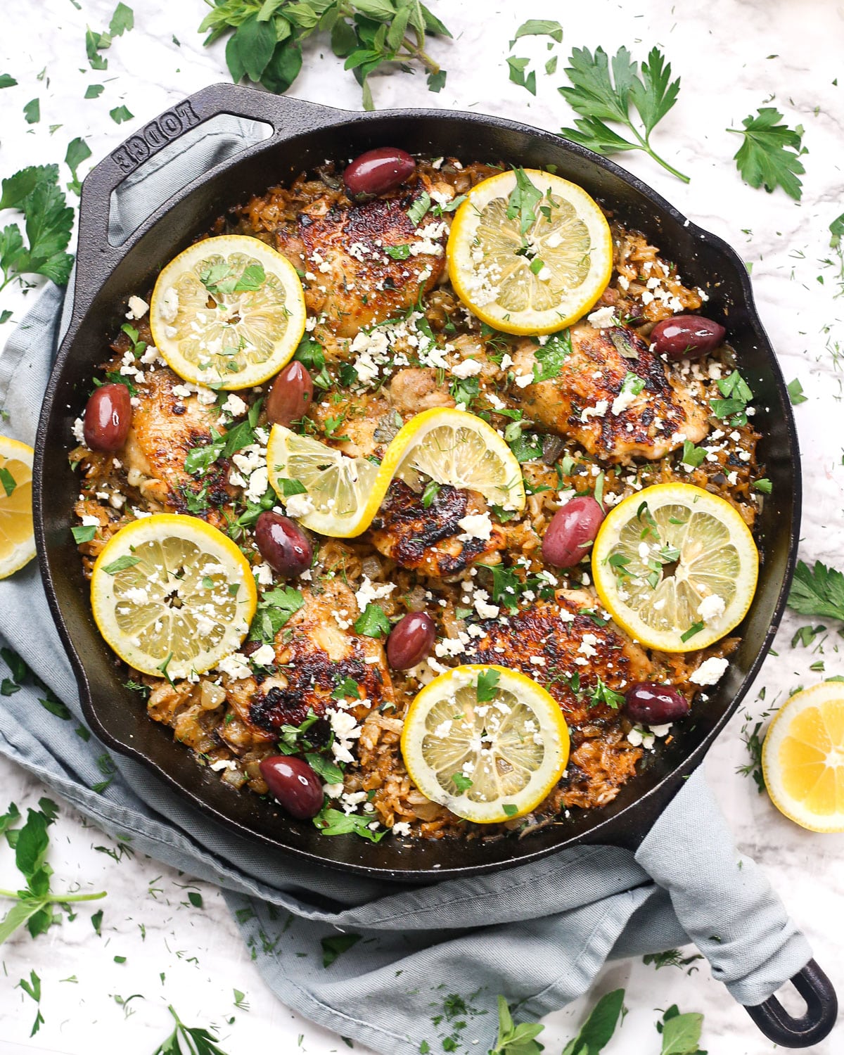 a skillet of mediterranean chicken and rice topped with lemons, herbs, and feta cheese.
