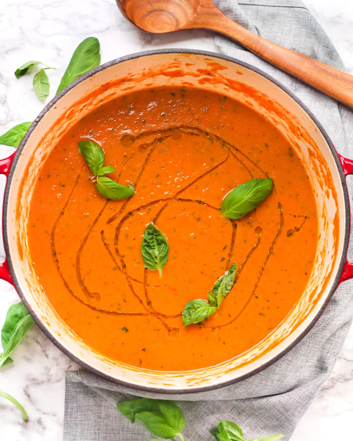 overhead photo of a large pot of creamy roasted tomato soup topped with fresh basil and a drizzle of oil