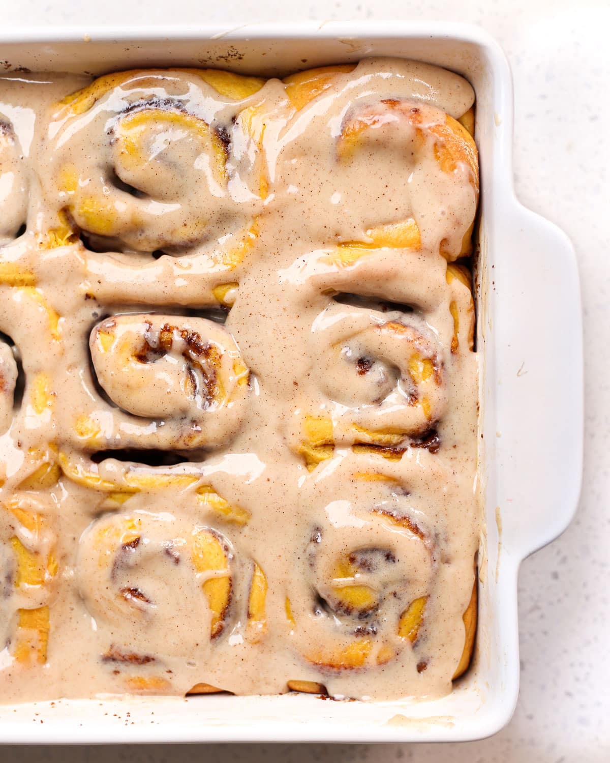 closeup of Pumpkin Spice Cinnamon Rolls in a baking dish covered with icing